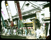 People on street in traditional dress outside building decorated with large banners, lanterns and signs.
