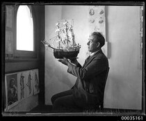 Man holding up a model of 16th century ship, 23 June 1934